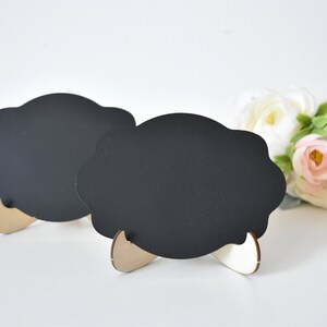 May include: Two black chalkboard signs with scalloped edges and wooden stands. The signs are blank and ready to be written on.