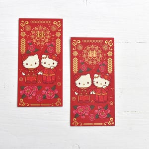 May include: Two red envelopes with gold accents and a floral design. The envelopes feature a cartoon couple of Hello Kitty characters dressed in traditional Chinese wedding attire. The text on the envelopes reads "囍" which means "double happiness" in Chinese.