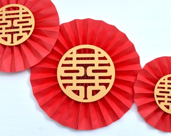 May include: Three red paper fans with gold double happiness symbols in the center. The fans are arranged in a row, with the largest fan in the center and the smallest fan on the right.