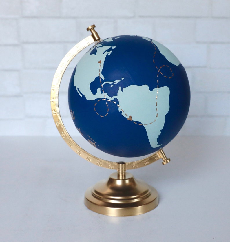 Puede incluir: Un globo terr&aacute;queo azul con un soporte dorado. El globo tiene un mapa del mundo azul claro con l&iacute;neas doradas y corazones.