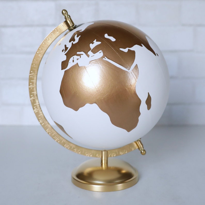 Puede incluir: Un globo terr&aacute;queo dorado y blanco con un soporte dorado. El globo tiene un fondo blanco con continentes dorados.