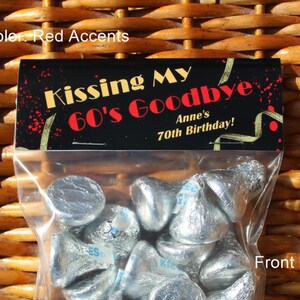 May include: A clear plastic bag filled with silver foil-wrapped chocolate kisses. The bag has a black label with gold and red accents that reads "Kissing My 60's Goodbye Anne's 70th Birthday!"
