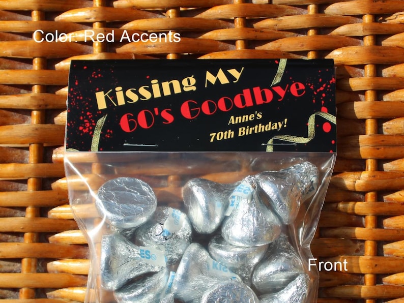May include: A clear plastic bag filled with silver foil-wrapped chocolate kisses. The bag has a black label with gold and red accents that reads "Kissing My 60's Goodbye Anne's 70th Birthday!"