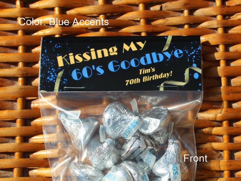 May include: A black and gold favour bag with a blue accent, featuring the text "Kissing My 60's Goodbye" and "Tim's 70th Birthday!" The bag is filled with silver foil-wrapped chocolate kisses.
