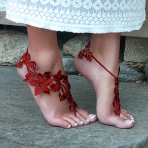 May include: Red lace barefoot sandals with floral designs. The sandals are tied around the ankle and have a delicate, feminine look.