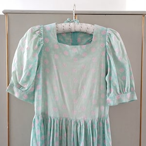 May include: A light blue dress with a square neckline and short puffed sleeves. The dress is covered in a delicate pink floral pattern.