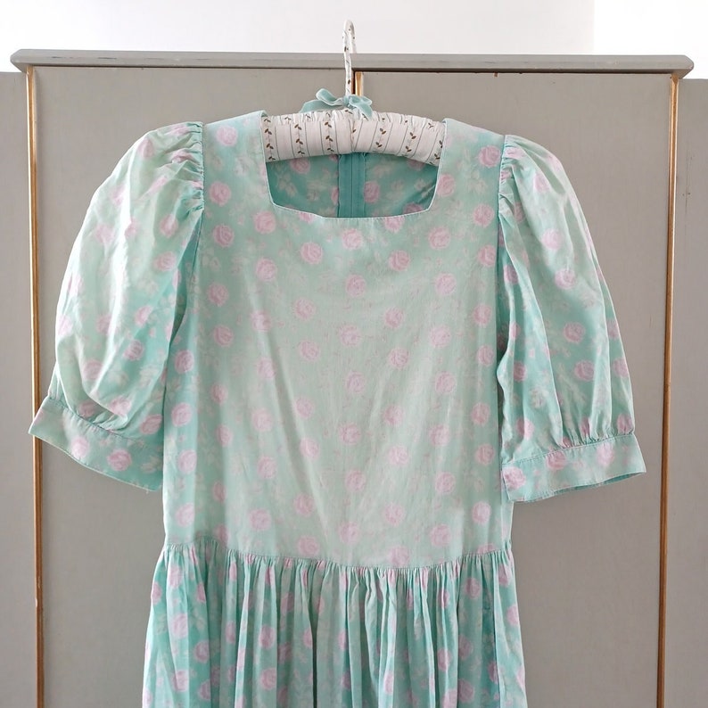 May include: A light blue dress with a square neckline and short puffed sleeves. The dress is covered in a delicate pink floral pattern.