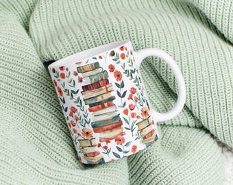 May include: White ceramic mug featuring a floral design and a stack of books printed on it. The mug is resting on a green knitted blanket.