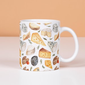 Puede incluir: Taza de cerámica blanca con un patrón repetido de diferentes quesos, como brie, cheddar y queso azul, con ramitas de romero. La taza tiene un asa blanca y está sobre un fondo neutro.