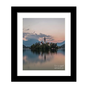 Puede incluir: Fotograf&iacute;a enmarcada de un paisaje esc&eacute;nico con una iglesia en una peque&ntilde;a isla en un lago. La imagen est&aacute; enmarcada en negro, con el lago reflejando el cielo y las estructuras de la isla. El cielo tiene suaves tonos rosados y azules.