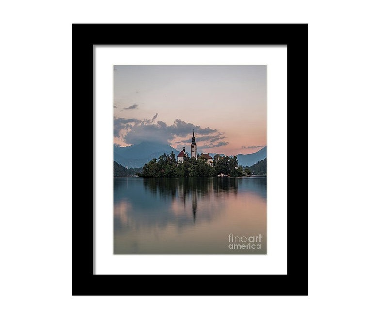 Puede incluir: Fotograf&iacute;a enmarcada de un paisaje esc&eacute;nico con una iglesia en una peque&ntilde;a isla en un lago. La imagen est&aacute; enmarcada en negro, con el lago reflejando el cielo y las estructuras de la isla. El cielo tiene suaves tonos rosados y azules.