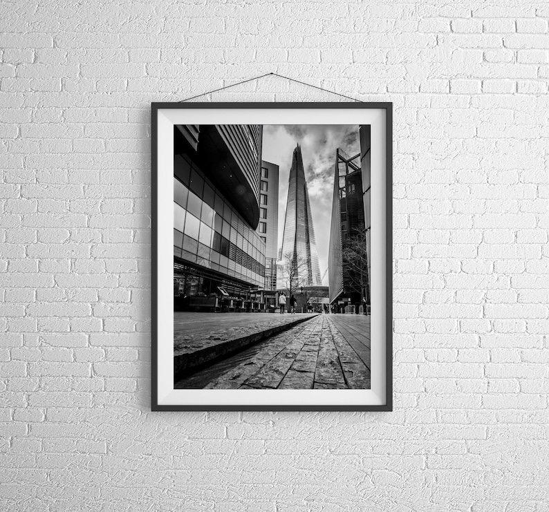 May include: A black and white photograph of the Shard, a tall skyscraper in London, England. The building is seen from a street level perspective, with other buildings in the background.