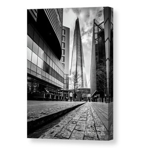 May include: A black and white photograph of a tall skyscraper in London, England. The building is surrounded by other buildings and a cobblestone street.