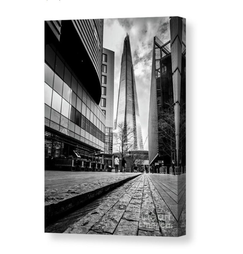 May include: A black and white photograph of a tall skyscraper in London, England. The building is surrounded by other buildings and a cobblestone street.