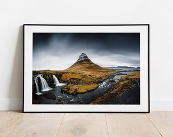 May include: A dramatic landscape photograph of a mountain peak with a waterfall in the foreground. The mountain is covered in snow and the sky is dark and stormy. The waterfall is flowing over rocks and into a river.