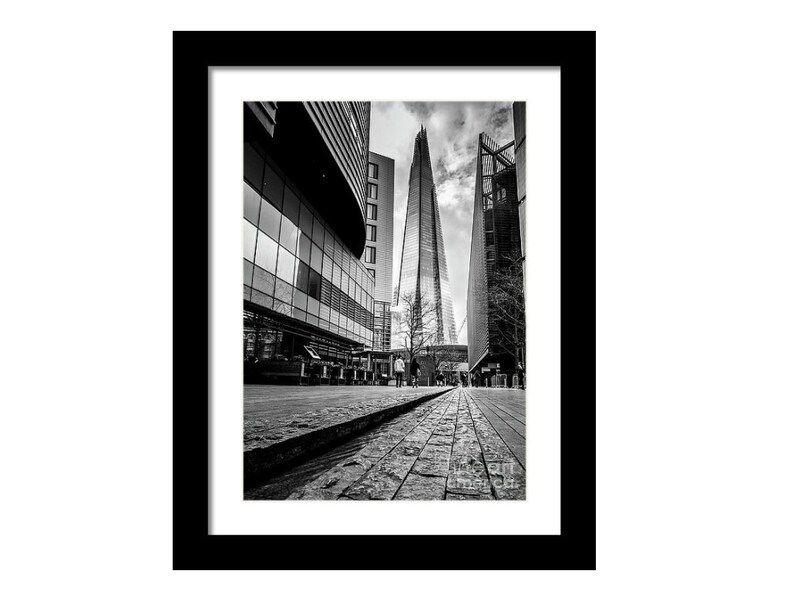 May include: A black and white photograph of a tall, modern skyscraper in London, England. The building is surrounded by other buildings and a paved street.
