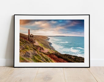 Könnte beinhalten: Ein Schwarzweißfoto eines verwitterten Steinbaus mit einem roten Backsteinkamin auf einer Klippe mit Blick auf ein stürmisches Meer. Der Himmel ist eine Mischung aus Blau, Grau und Rosa.