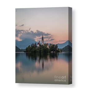 Puede incluir: Impresi&oacute;n en lienzo de un paisaje esc&eacute;nico con una iglesia en una isla en un lago. La imagen captura una serena puesta de sol con suaves tonos rosados y azules que se reflejan en el agua. Se ven monta&ntilde;as al fondo.