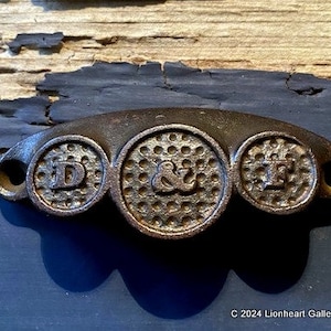 May include: A cast iron drawer pull with three round knobs. The knobs are embossed with the letters "D", "&", and "F".