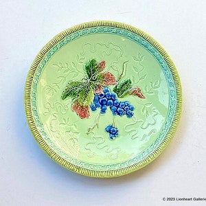 May include: A green ceramic plate with a raised design of grapes and leaves. The plate has a yellow and blue border.