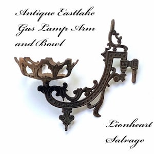 May include: Antique Eastlake gas lamp arm and bowl, made of cast iron with intricate details. The arm is curved and has a decorative design. The bowl is round and has a scalloped edge. The piece is in good condition and has a dark brown patina.