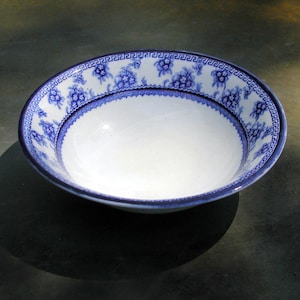 May include: A white ceramic bowl with a blue and white floral pattern around the rim. The bowl is empty and sitting on a gray surface.