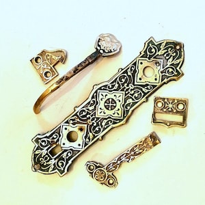 May include: Antique brass door hardware set with intricate floral designs and a black enamel finish. The set includes a door handle, a latch, and two decorative pieces.