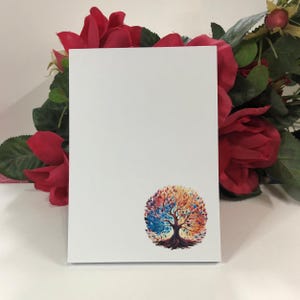 May include: A white notepad with a colorful tree illustration. The tree has blue, red, orange, and yellow leaves. The tree is in a circle shape.