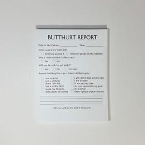 May include: A white notepad with the title "BUTTHURT REPORT" printed in black. The notepad includes fill-in sections for the date, time, and reasons for the report, with checkboxes for various options. The notepad is designed for humorous use.