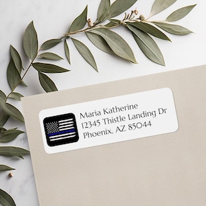 May include: White rectangular address label with the text "Maria Katherine 12345 Thistle Landing Dr Phoenix, AZ 85044". The label features a black and white American flag with a blue line.