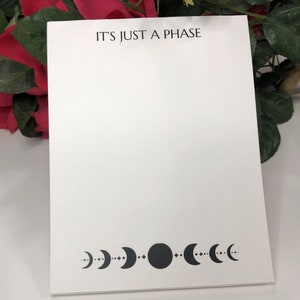 May include: White notepad with the text "IT'S JUST A PHASE" printed at the top. The bottom of the notepad features a black moon phase design.