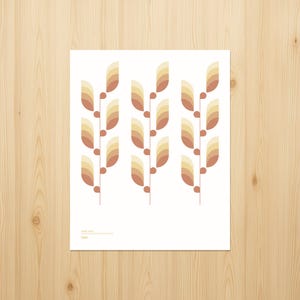 May include: A white poster with a repeating pattern of stylized wheat stalks. Each stalk features layered, fan-shaped elements in shades of brown, tan, and yellow, with small red-brown dots. The poster is on a light wood surface.
