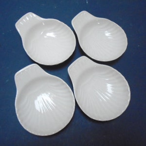 May include: Set of four white ceramic shell-shaped bowls. The bowls have a textured, ribbed surface and a slightly curved lip.