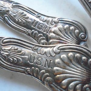 Peut inclure: Deux cuillères en argent avec des manches ornés. Les manches sont gravés des lettres "U.S.N."