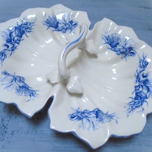 May include: A white ceramic serving dish with a blue and white seashell design. The dish has a handle in the centre and is divided into two sections.
