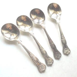 Könnte beinhalten: Set aus vier versilberten Suppenlöffeln mit verzierten Griffen. Die Löffel haben ein klassisches Design mit einer abgerundeten Schale und einem dekorativen Griff.