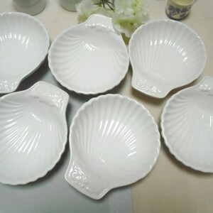 May include: Six white ceramic bowls shaped like seashells. The bowls are all the same size and have a smooth, glossy finish.