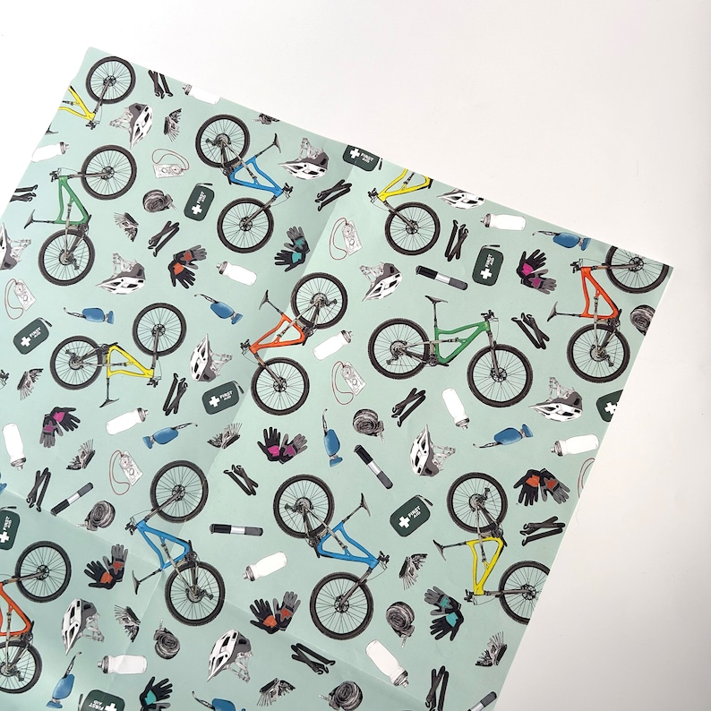 May include: A green, blue, and orange mountain bike pattern on a light green background. The pattern includes various cycling accessories, such as helmets, water bottles, and tools.
