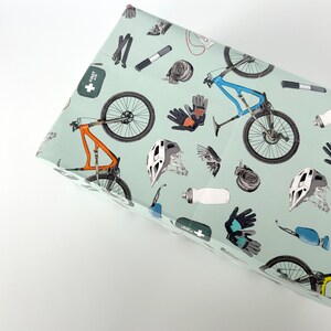 May include: A green and white gift wrap with a mountain bike, helmet, gloves, and other cycling accessories. The text "First Aid Kit" is printed on the wrapping paper.