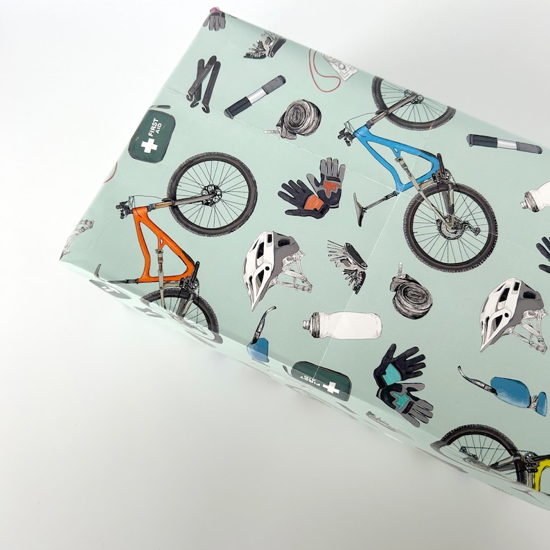 May include: A green and white gift wrap with a mountain bike, helmet, gloves, and other cycling accessories. The text "First Aid Kit" is printed on the wrapping paper.