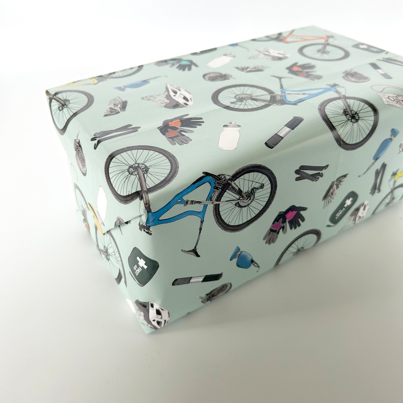 May include: A light blue gift wrap with a repeating pattern of mountain biking accessories, including bicycles, helmets, gloves, and water bottles.