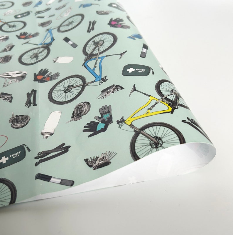 May include: A green wrapping paper with a repeating pattern of mountain bikes, tools, and first aid kits. The bikes are in various colors, including blue, yellow, and black. The tools include wrenches, tire levers, and a chain tool. The first aid kit is green with a white cross.