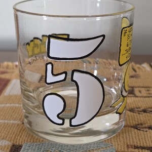 May include: A clear glass tumbler with a white outlined number "5" and yellow cartoon graphics. The glass has text that reads "If you is not 6.7...then you". The glass is on a patterned surface.