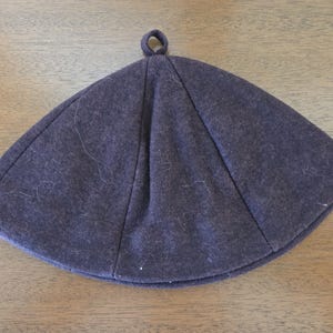 May include: A dark gray, brimless hat with a rounded crown and a small loop at the top. The hat is made of a soft, felt-like material and has visible seams. The hat is likely for cold weather.