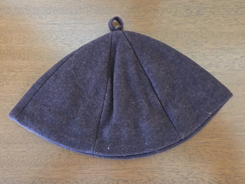 May include: A dark gray, brimless hat with a rounded crown and a small loop at the top. The hat is made of a soft, felt-like material and has visible seams. The hat is likely for cold weather.
