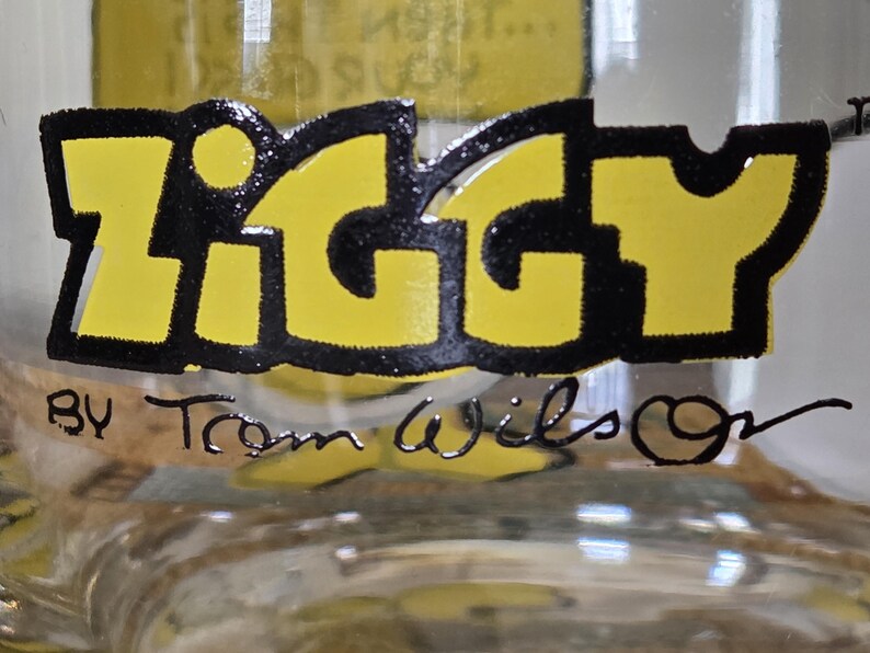 May include: Close-up of a clear glass object with the word "IGGY" in large yellow letters outlined in black. Below the word is the text "BY Tom Wilson" in black script.