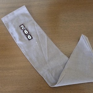 May include: A folded, light gray fabric item with the numbers "266" printed on a small rectangular patch. The fabric is lying on a wooden surface, with the item folded into a V-shape.