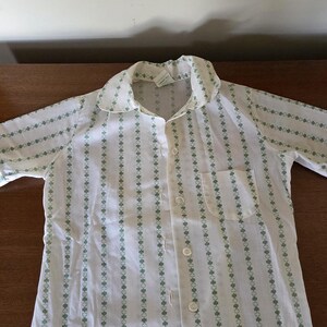 May include: White button-down shirt with a green clover pattern. The shirt has a collar, a chest pocket, and is buttoned up. The pattern is vertical stripes of green clovers.