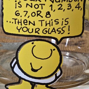 May include: A clear glass with a yellow cartoon character sticker. The sticker has a speech bubble with the text: "IF YOUR NUMBER IS NOT 1,2,3,4, 6,7, OR 8...THEN THIS IS YOUR GLASS!"