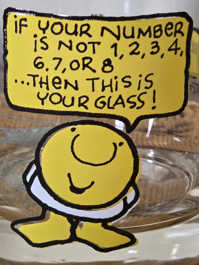 May include: A clear glass with a yellow cartoon character sticker. The sticker has a speech bubble with the text: "IF YOUR NUMBER IS NOT 1,2,3,4, 6,7, OR 8...THEN THIS IS YOUR GLASS!"